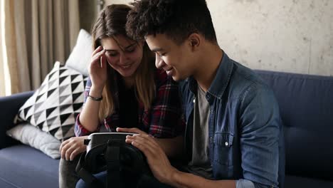 young mulatto guy turns vr-headset on and helps his girlfriend to put it on.