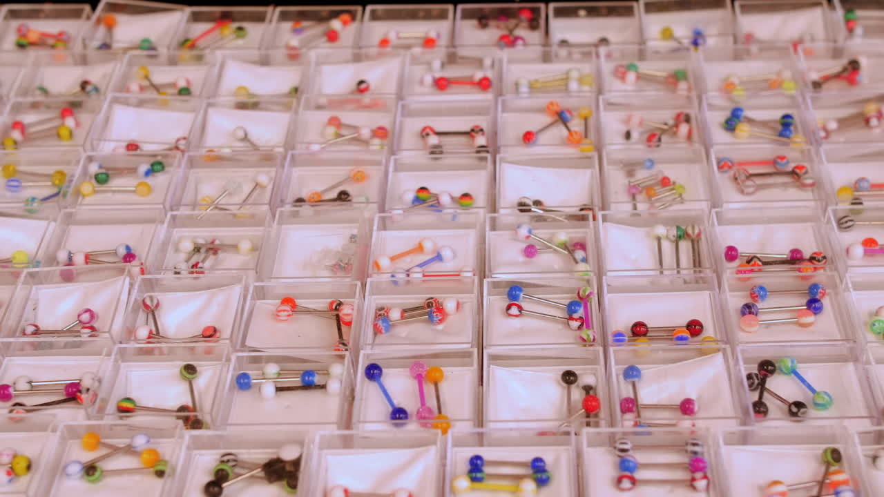 Colorful barbell belly and nose piercings displayed in individual compartments, showcasing a variety of vibrant patterns and designs.