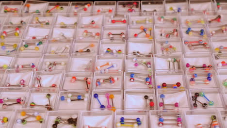 Colorful barbell belly and nose piercings displayed in individual compartments, showcasing a variety of vibrant patterns and designs.