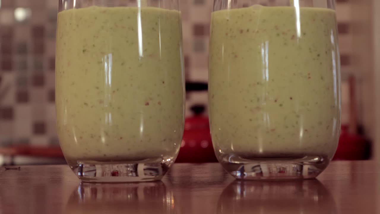 A close up shot of two glasses on the counter top, a smoothie fruit and veg blend mix is poured on both glasses.