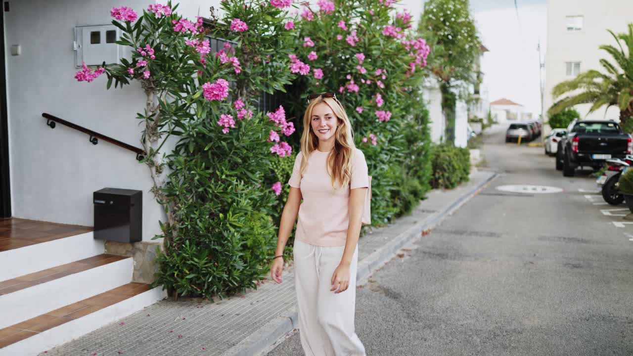 Jovem mulher loira caminhando e sorrindo em uma rua ensolarada com flores