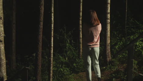 sad young woman in home clothes looks thoughtfully into dark thickets of forest. lady enjoys nature and thinks about life while standing near stairs of house