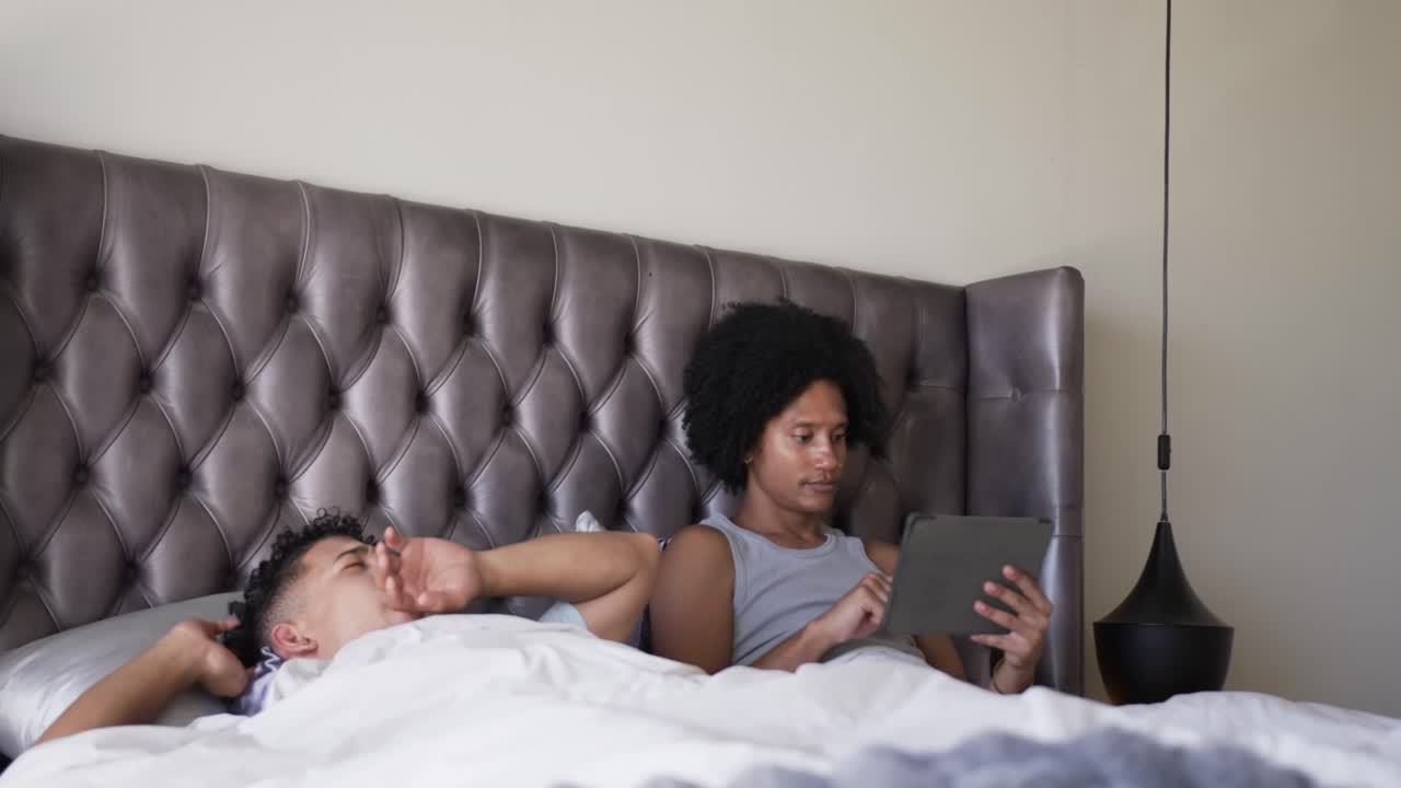 Left man waking in bed, seeking attention, right man tapping tablet, glancing, focusing on tech