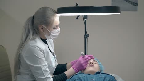 professional cosmetician holds tattoo gun and lady forehead