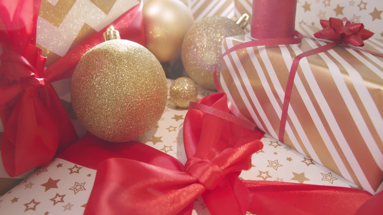 Regali di Natale incartati in oro, bianco e rosso, illuminati da una luce allegra e brillante.