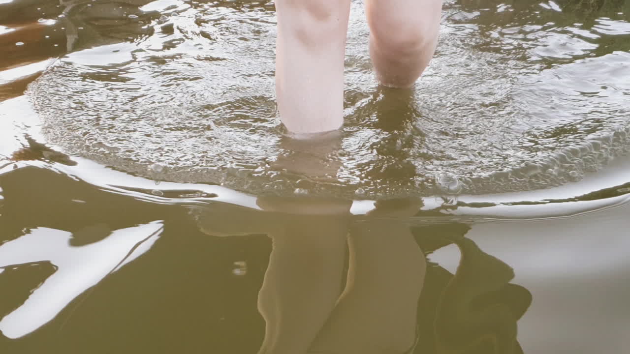 White legged girl steps into muddy water, walks through water approaching
