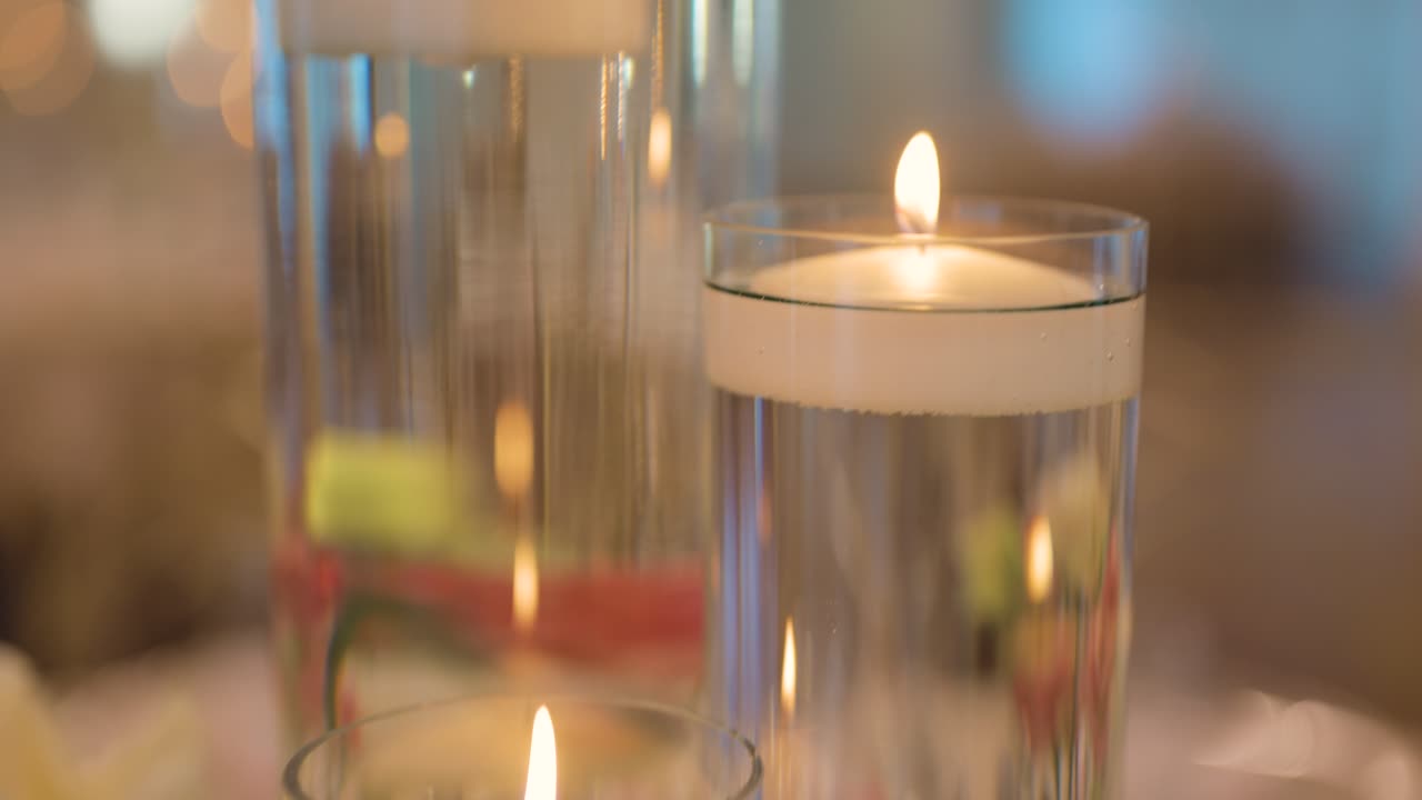 Gros plan sur d'élégantes bougies flottantes placées dans des vases en verre transparent remplis d'eau, créant une ambiance chaleureuse et intime.