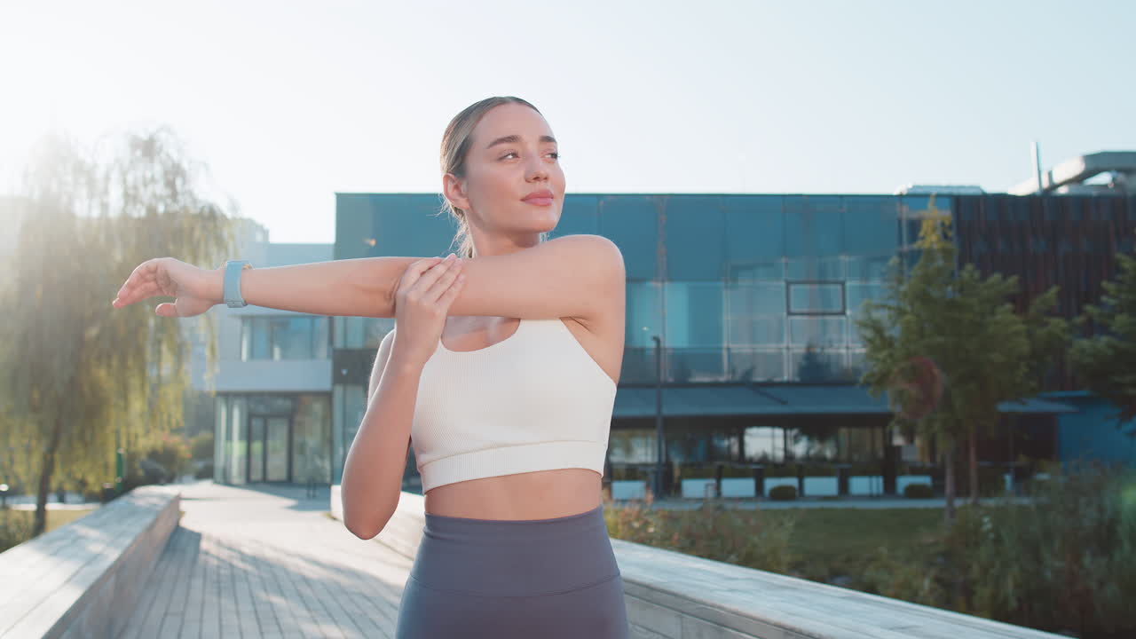 Caucasian sporty young woman runner stretching arms warm up before jogging in city park on sunny day