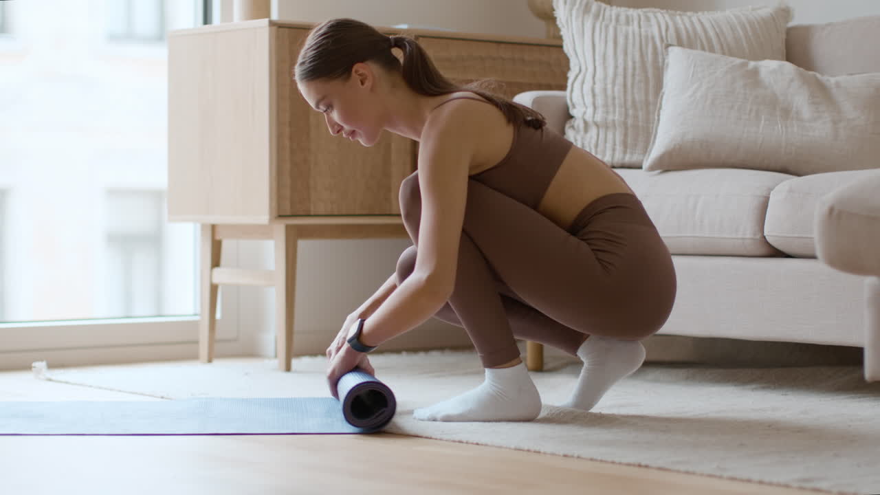 mujer enrollando una alfombra de yoga en casa