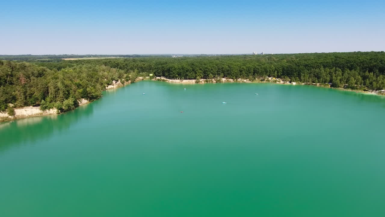 Smooth turquoise surface of water in former quarry. Drone footage over the lake and forest around it. Circle movement.