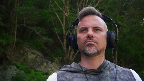 man standing and looking while listening to music with headphones on, in nature