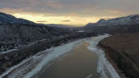 snowy thompson river: a winter wonderland bathed in a dramatic sunset sky