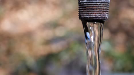 Close-up-shot-of-a-rusty-fountain-with-crystal-clear-water-in-slow-motion