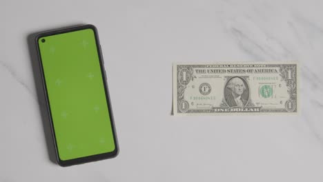 Overhead-Currency-Shot-Of-Hand-Grabbing-US-1-Dollar-Bill-Next-To-Green-Screen-Mobile-Phone