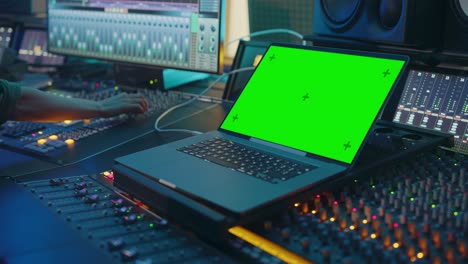 moderno escritorio de control de estudio de grabación de música con pantalla verde llave croma portátil, ecualizador, mezclador y otros equipos profesionales. conmutadores, botones, faders, deslizadores. grabar, reproducir canciones. primer plano