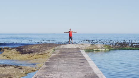 Senior-african-american-man-exercising-raising-hands-by-the-sea