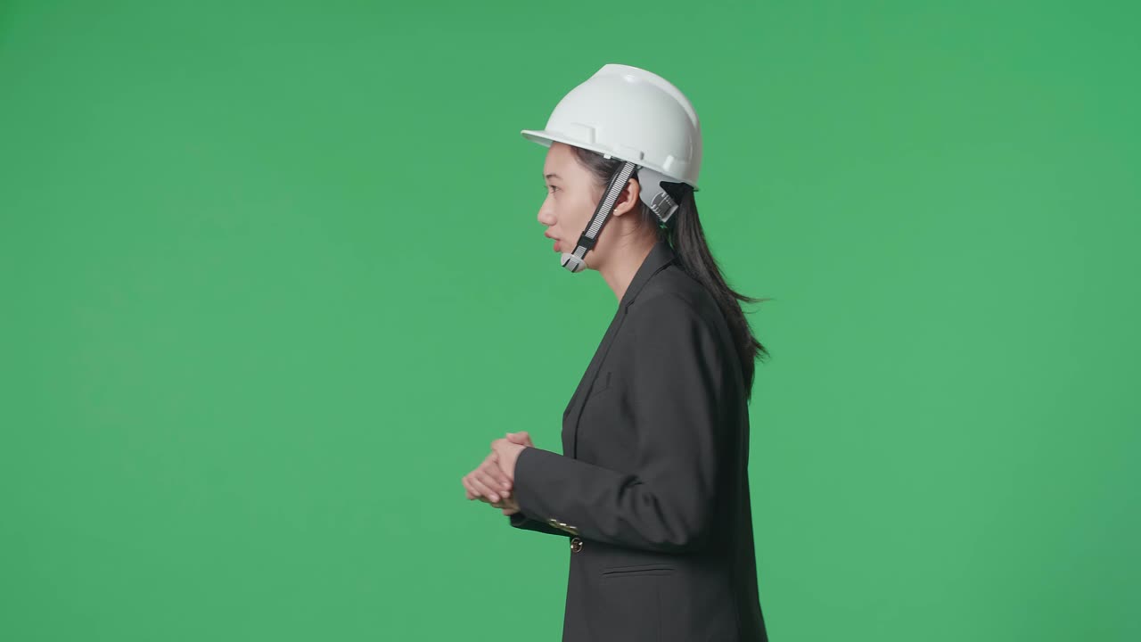 Side View Of Smiling Asian Female Engineer Talking While Walking In The Green Screen Studio