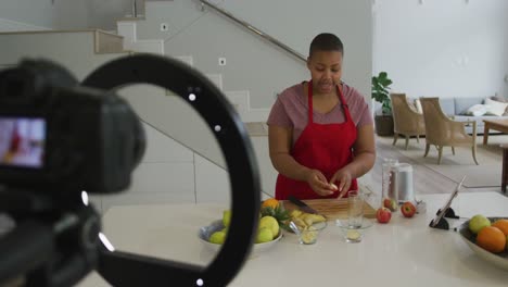 feliz mujer afroamericana de talla grande con delantal, haciendo un vlog de cocina con cámara en la cocina
