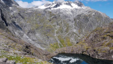 inclinación aérea hacia abajo tiro montañas masivas con pico nevado que se refleja en la superficie natural del lago de montaña durante la luz del sol - caminata de sillín gertrude en nueva zelanda