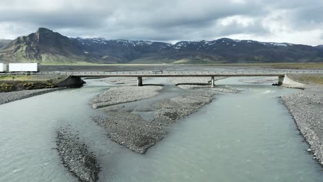 aerial flying under bridge crossing glacial river in iceland, truck on road