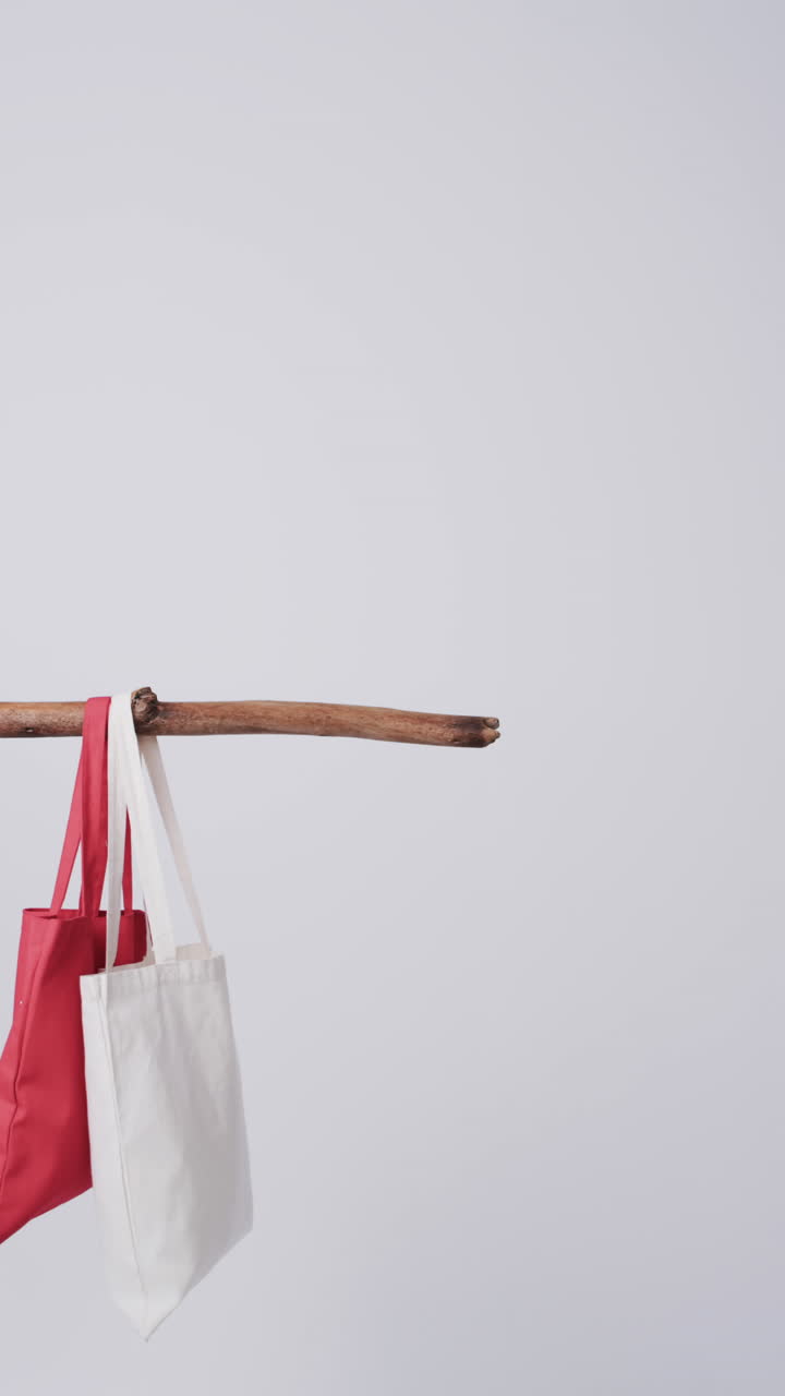 Vertical video of red and white canvas bag hanging from branch with copy space on white background