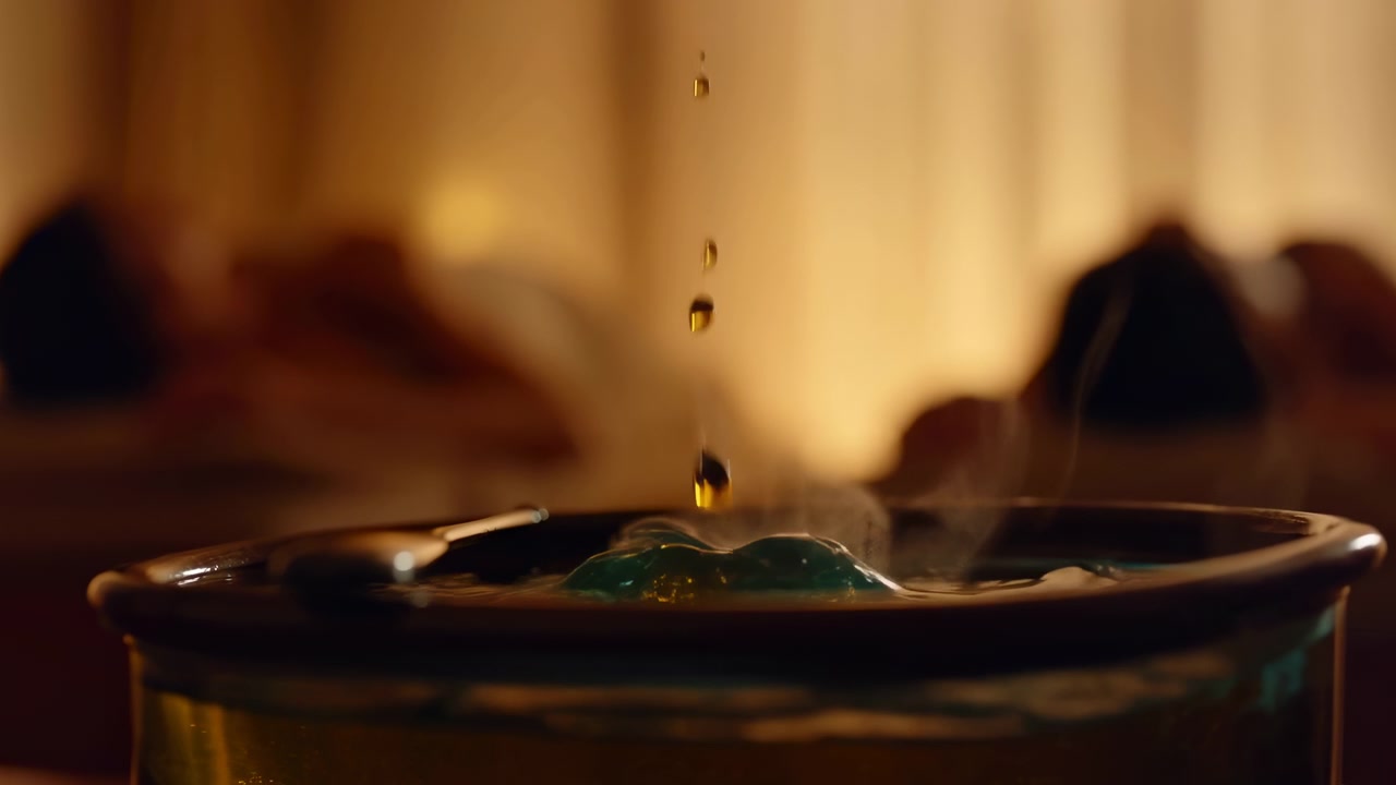 Nærbilde av en enkelt gyllen dråpe som faller ned i en klar glassbeholder, omgitt av myke ravtoner, uskarp bakgrunn og milde refleksjoner i en