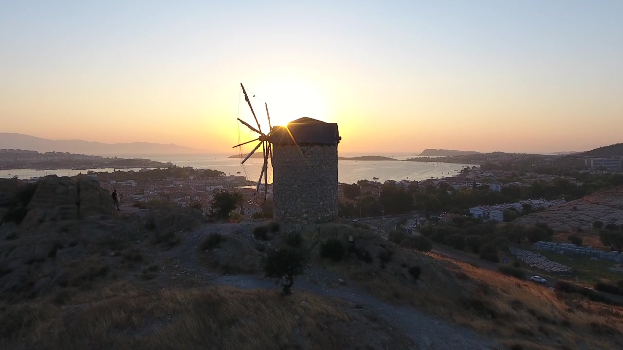 Moinho de Vento Antigo de Pedra com vista para uma cidade costeira ao pôr do sol