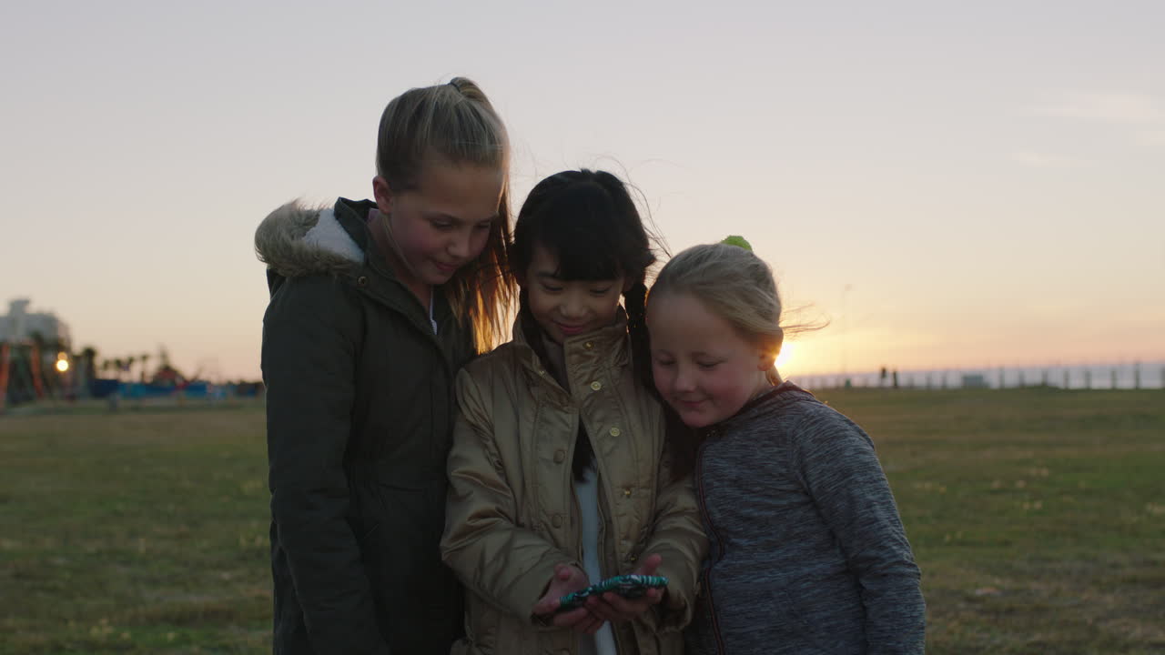 해가 지는 동안 야외 공원을 즐기는 스마트폰 카메라 기술을 사용하여 셀카 사진을 찍는 작은 소녀들의 초상화