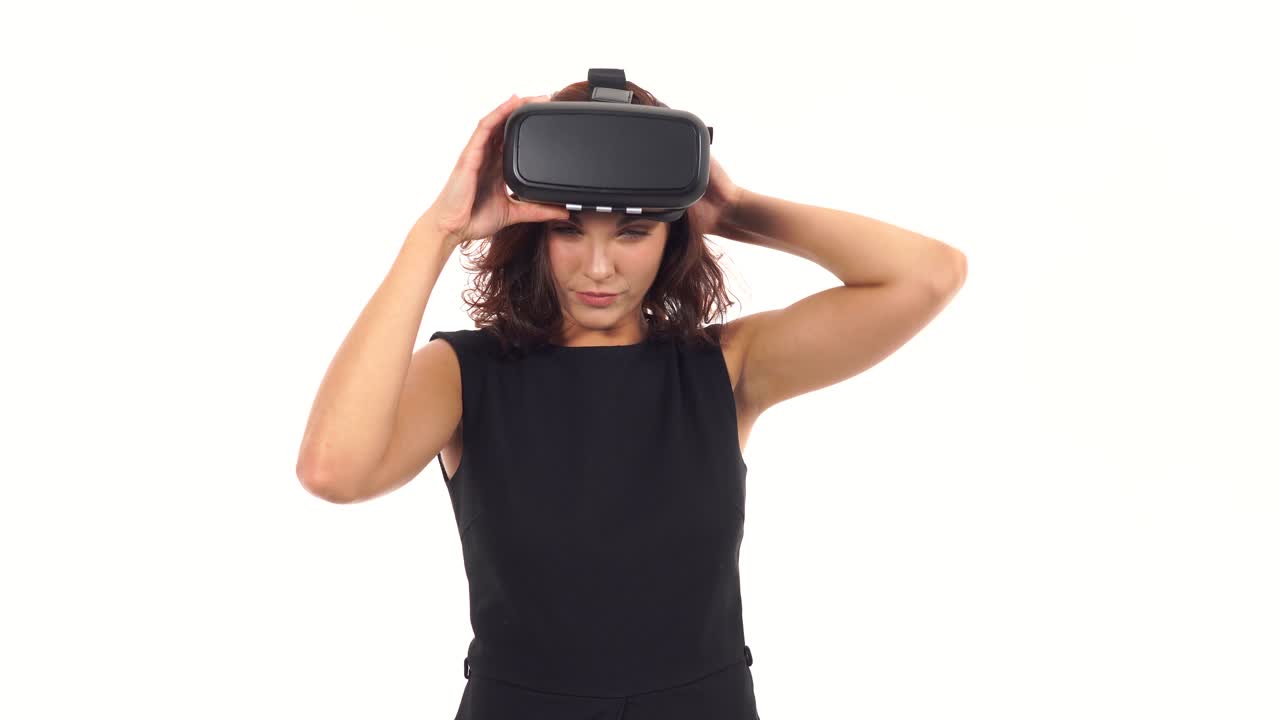 mujer joven atractiva en vestido negro tomando, mirando a su alrededor y luego quitando gafas de realidad virtual aislados sobre blanco