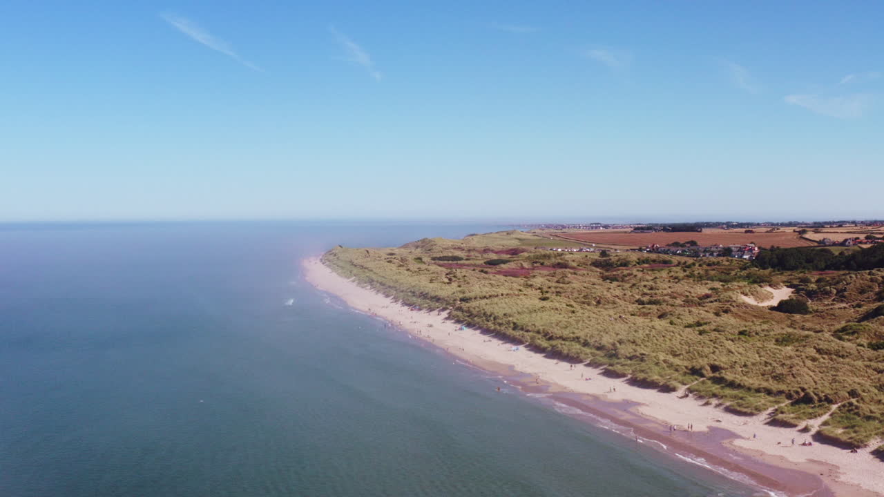 toma aérea desde lo alto, elevándose sobre una playa británica en un día de verano abrasador mientras las familias juegan debajo