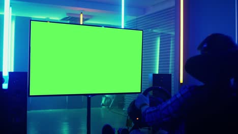 professional gamer sitting before green mock-up screen tv in the racing seat simulator cockpit with steering wheel and playing in car racing online video game.