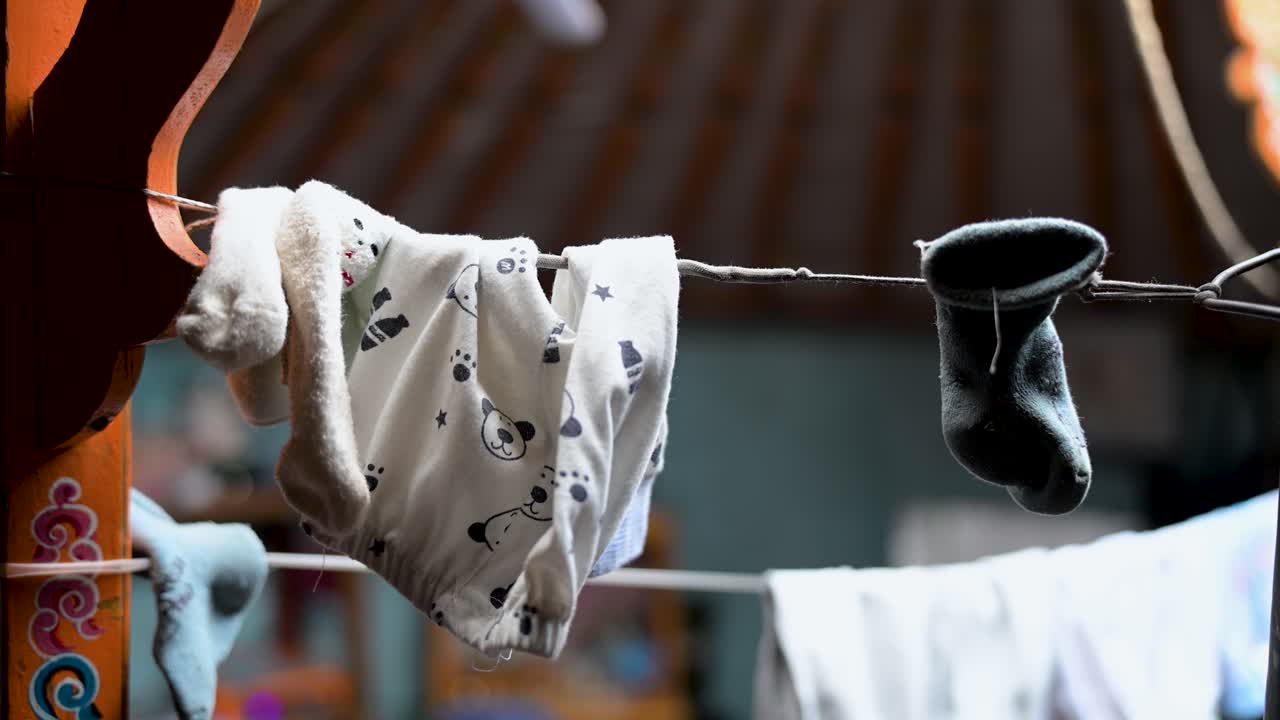 Baby clothes hang on a makeshift clothesline to dry inside a traditional nomadic ger in Mongolia. An authentic, intimate scene of daily domestic life and chores