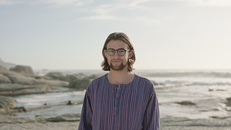 ritratto di un uomo carino che indossa occhiali su una spiaggia soleggiata che indossa una camicia a righe