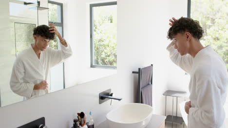 looking in mirror, person in bathrobe adjusting hair in modern bathroom