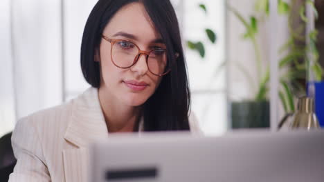 mujer concentrada con gafas trabajando en una computadora portátil en la oficina
