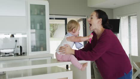 madre caucásica besándose mientras juega con su bebé en la cocina en casa