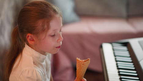 little girl with brown hair tied in ponytail sitting indoors happily eating ice cream cone next to piano keyboard, cozy atmosphere with slightly blurred background