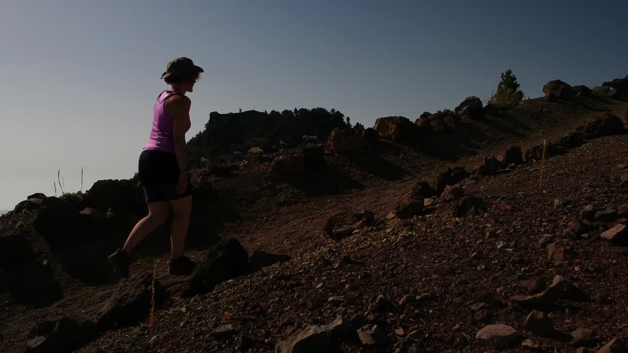 Aerial shot following a female explorer on top of a volcano, with an amazing sea of clouds in the background
