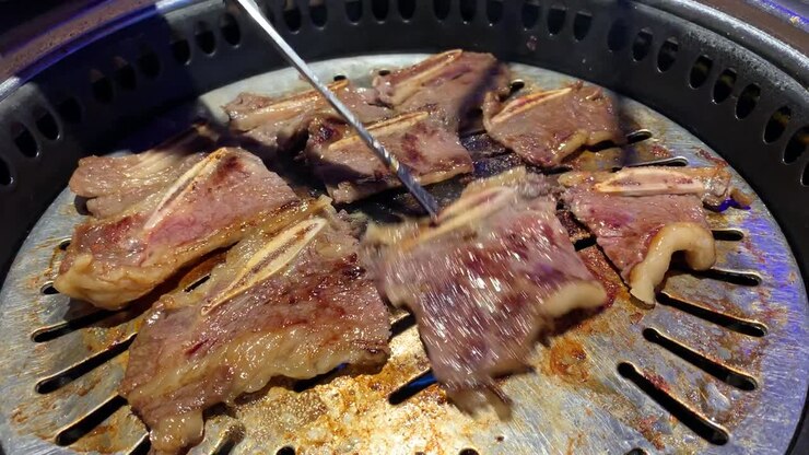 Costine di BBQ coreano che cuociono su una griglia rovente in acciaio inossidabile in un ristorante coreano