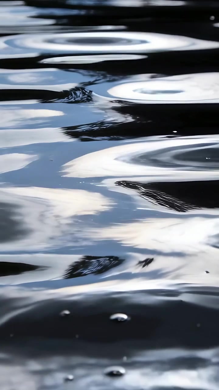 Вертикальное видео: Крупный план рябящей воды, реагирующей на капли, и меняющееся сине-белое небо над прудом.