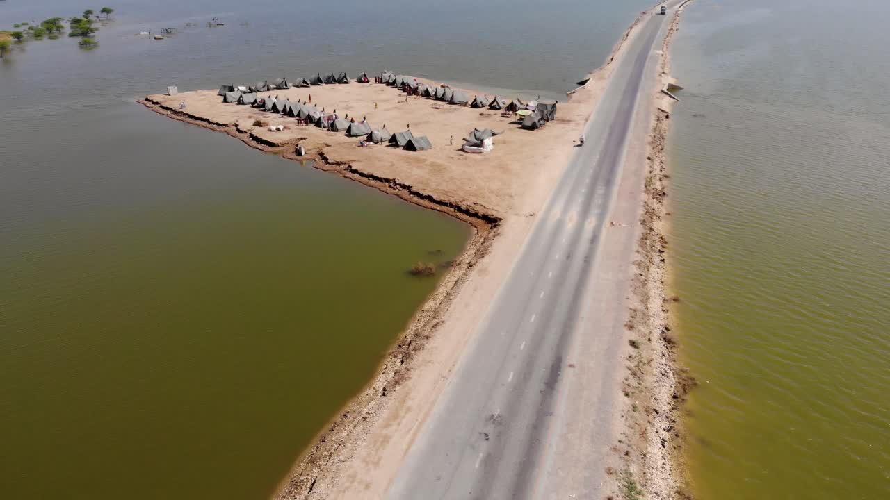 시골 자코바바드, 신드의 광대한 홍수로 둘러싸인 고가 도로 옆에 홍수 난민을 수용하기 위한 텐트가 있는 임시 캠프의 공중 전망