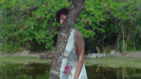 bonita chica de cabello rizado rojo caminando en un parque usando un vestido largo de flores con un estanque en el fondo