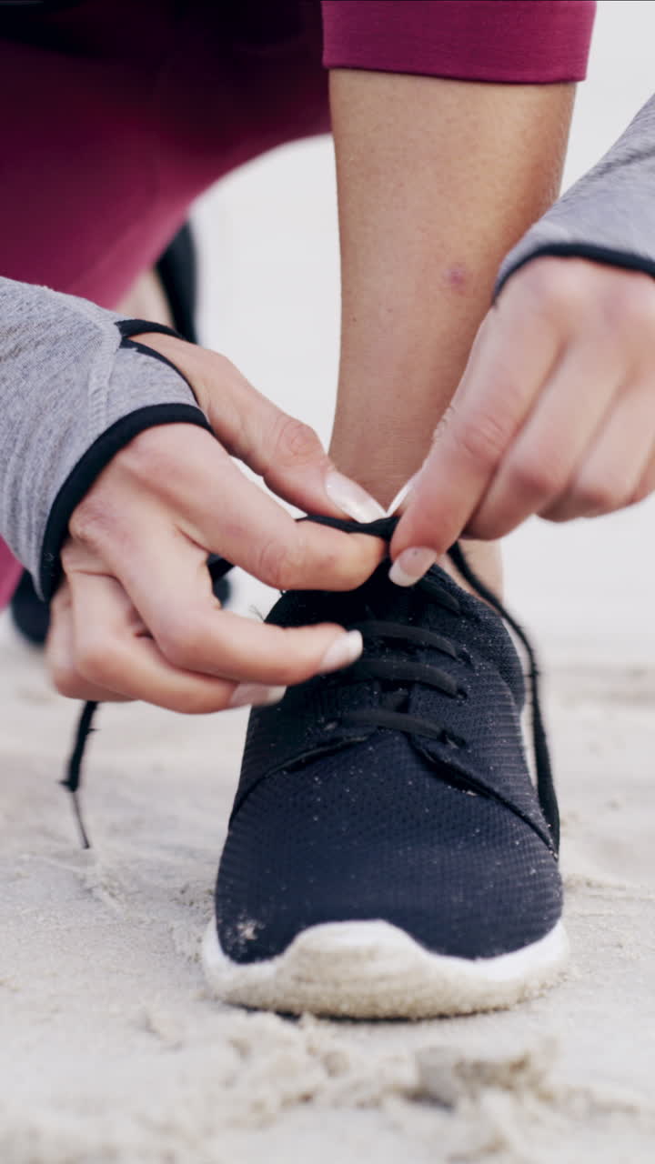 Primo piano delle mani che allacciano le scarpe da corsa nella sabbia
