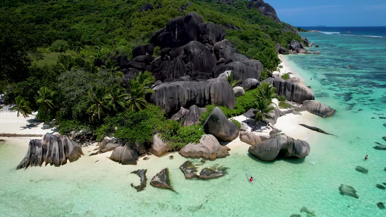 Veduta aerea della spiaggia Anse Source D'argent nelle Seychelles, con zoom su una donna in kayak con fondo trasparente.