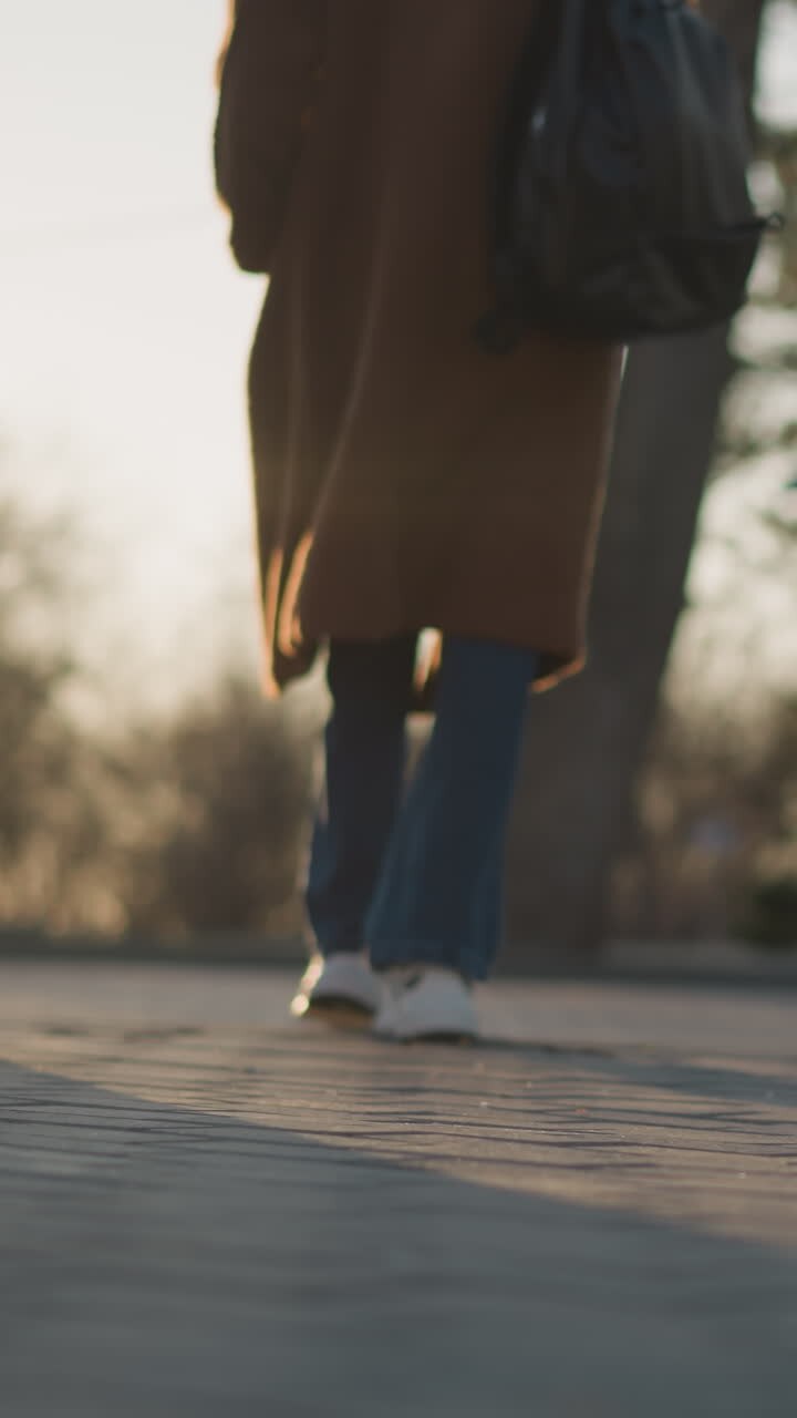 A girl walking in a blurred park, the shot begins with a focus on her legs and feet. The image captures the motion and solitude of the walk, with the background softly out of focus