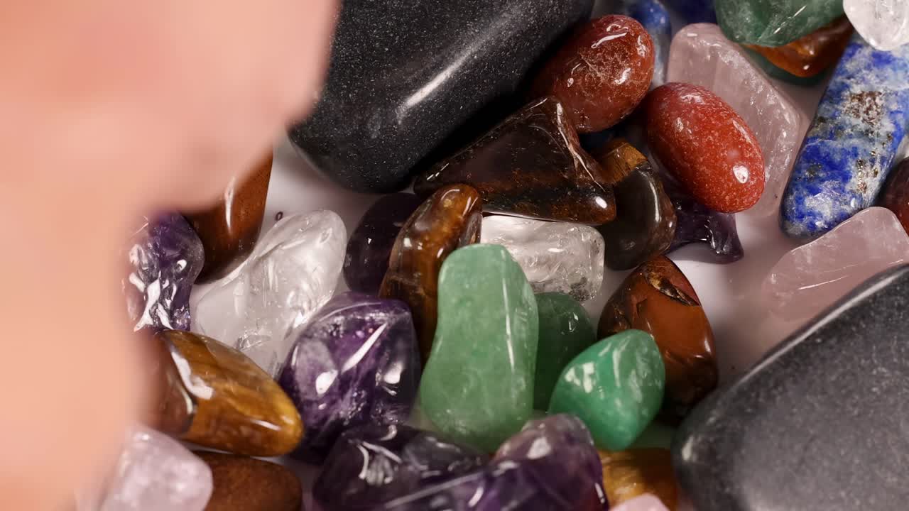 Detailed view of tweezers sorting vibrant gemstones on a white surface, highlighting texture and color.