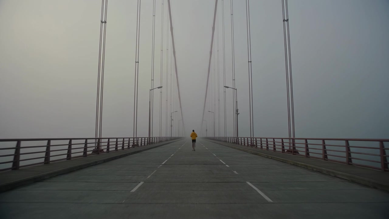 Running adult male starting and moving along center of suspension bridge, with yellow top in fog