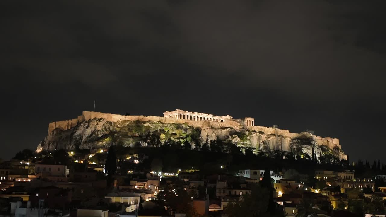 Athens,Time Laps of beautifully illuminated Acropolis at night time from a distance, with moving clouds above and shimmering lights