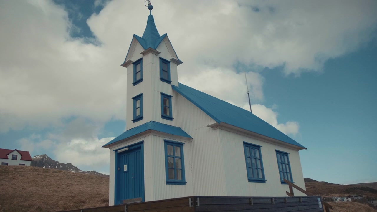 Chiesa bianca con tetto blu e campanile in un paesaggio rurale islandese