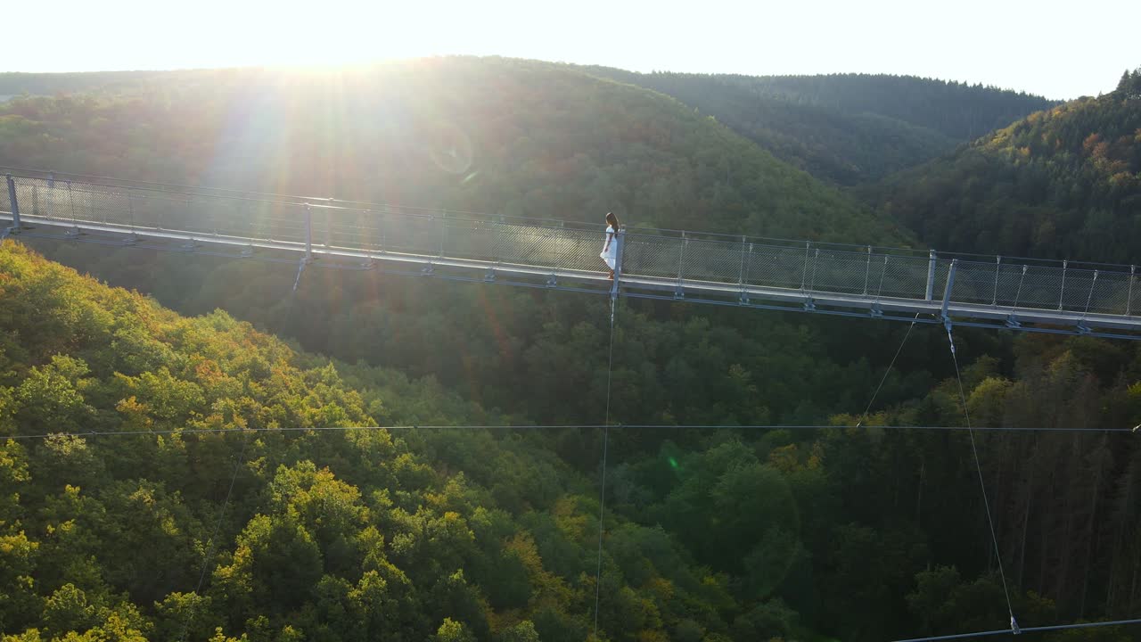 Aerial shot of young woman walking across Geierlay suspension bridge in Western Germany